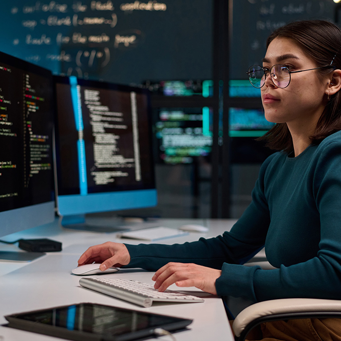 Side view portrait of young woman wearing glasses as cybersecurity engineer typing at computer keyboard and writing code 